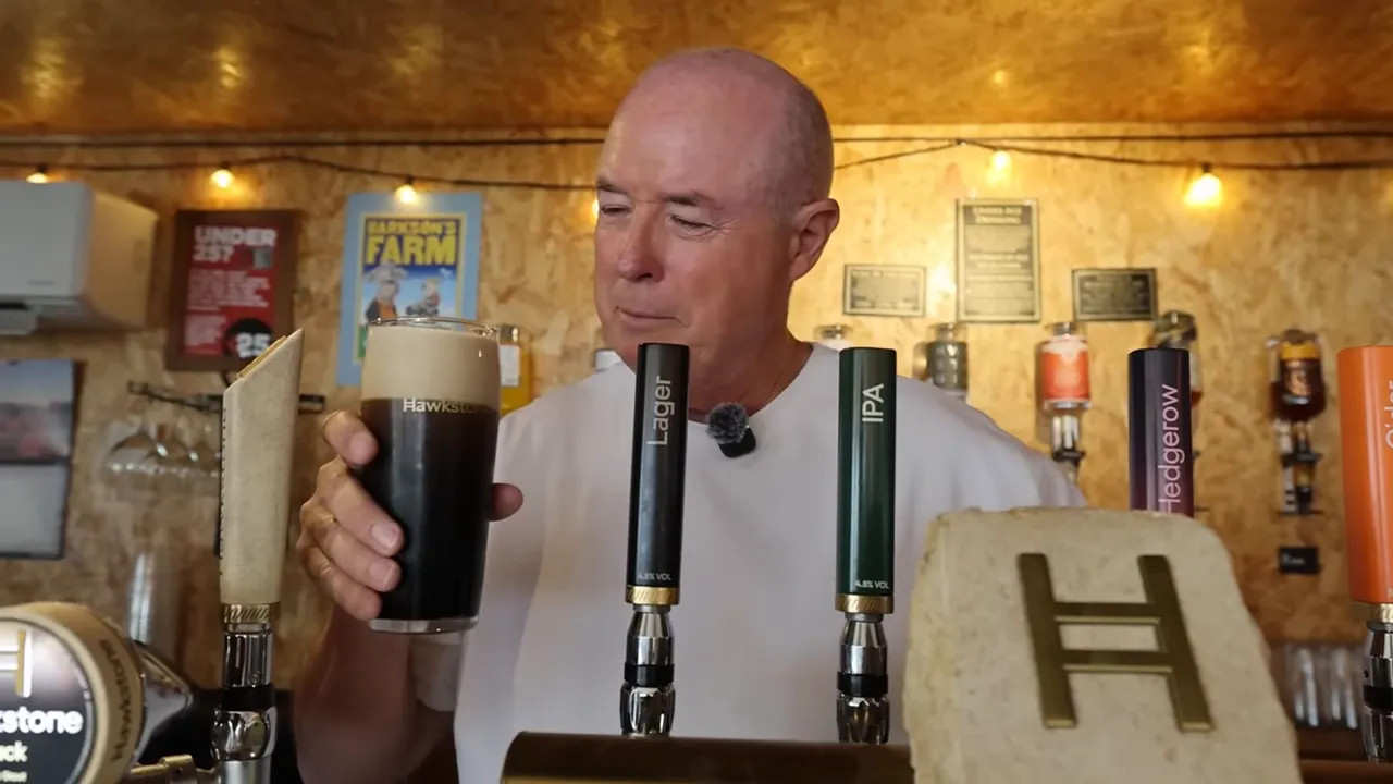 Pint of dark stout with a thick creamy head held in front of beer taps