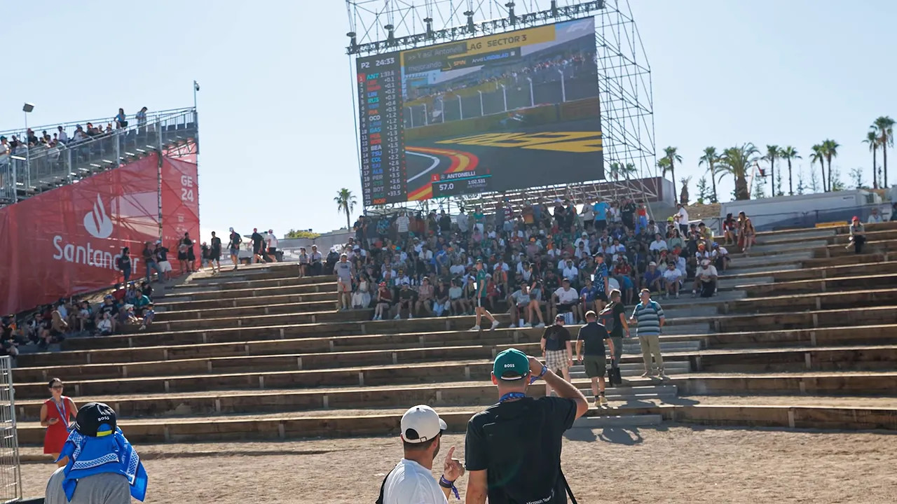 Concrete spectator steps leading to a large video screen with people gathered in the shade
