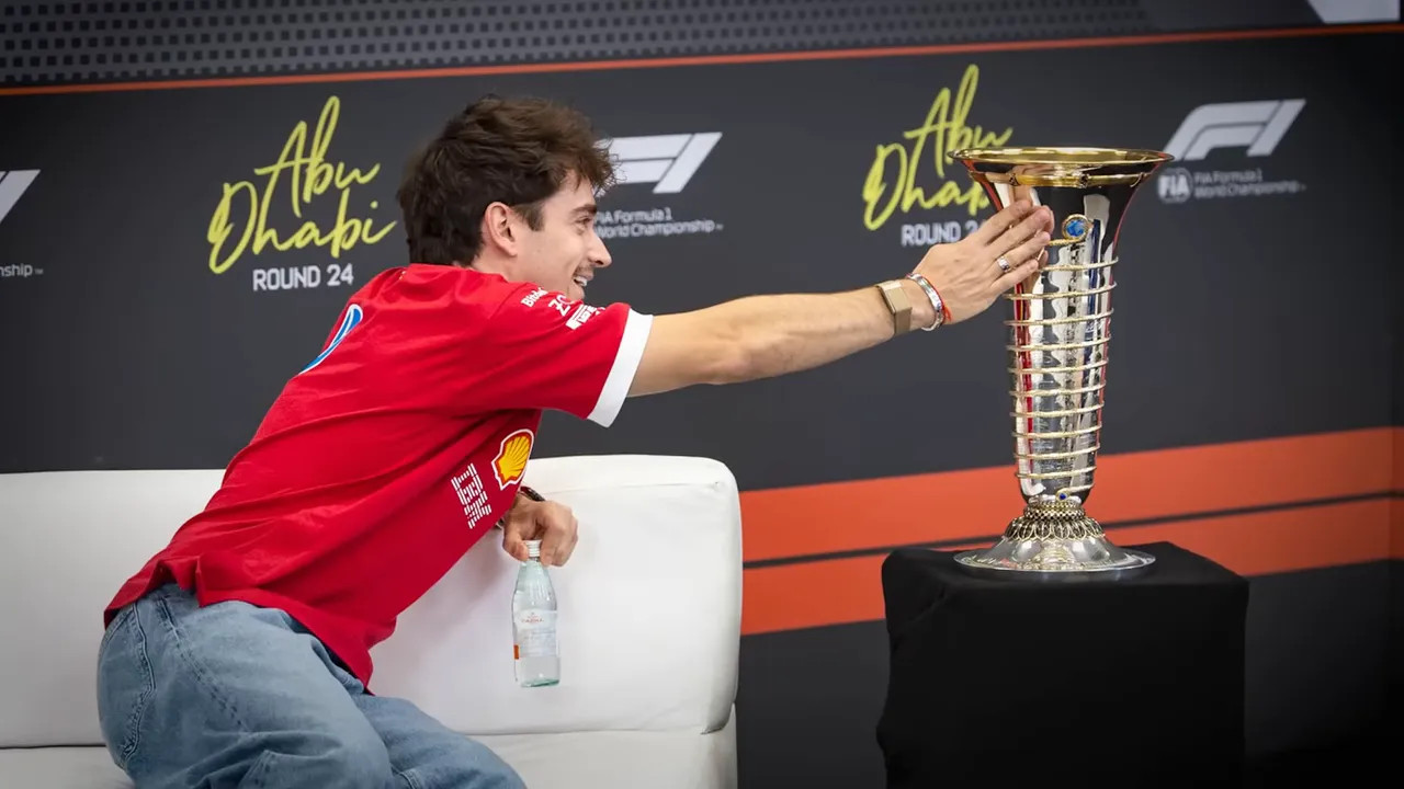Driver in red team shirt leaning from a sofa to touch the championship trophy at Abu Dhabi press conference