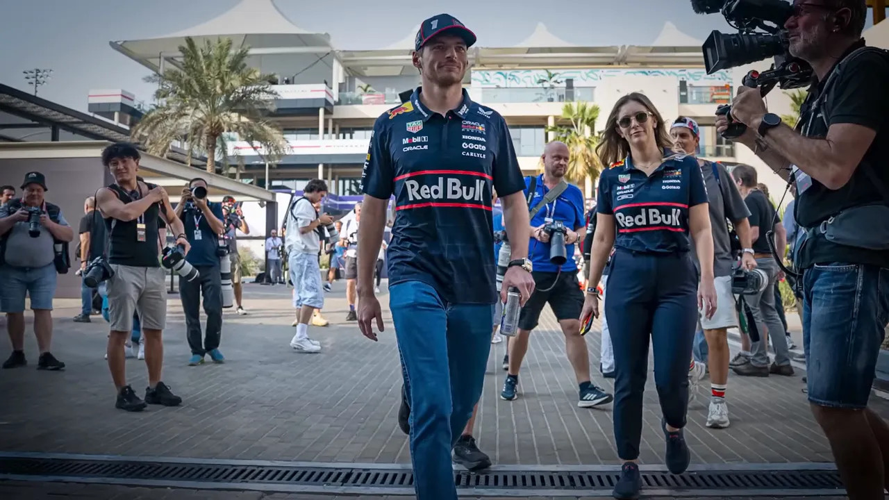 Formula 1 driver and team member walking through a crowded paddock while photographers and camera crews follow
