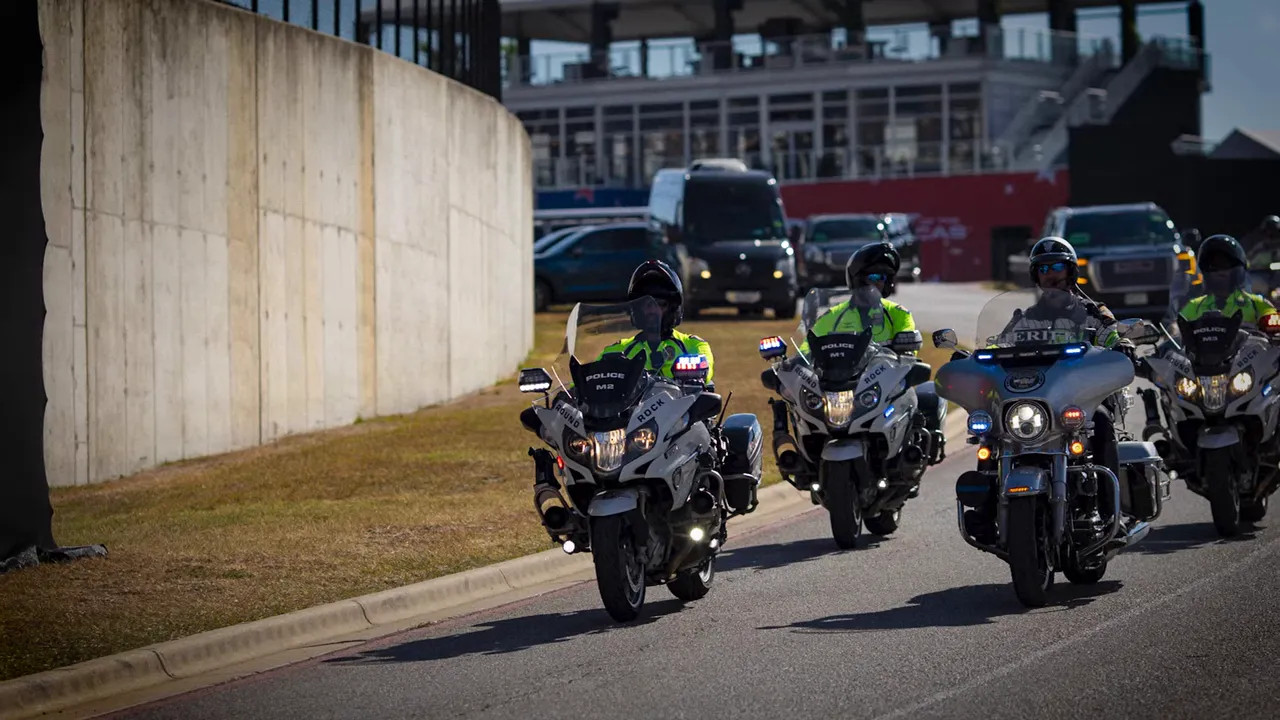 Several police motorcycles leading vehicles along a circuit access road