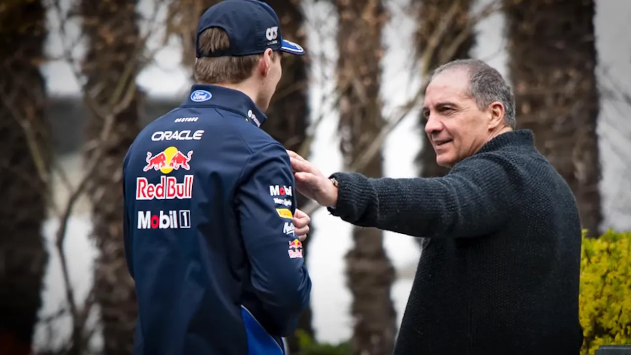 A person placing a hand on a driver's shoulder in the paddock, a warm greeting captured beside palm trees.
