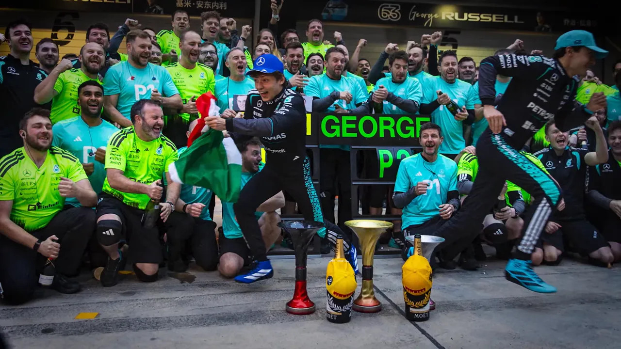 Podium scene with trophies in front, drivers jumping and the team cheering wildly behind them