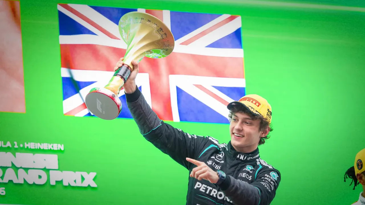 Young F1 driver raising a gold trophy on the podium with a union jack backdrop