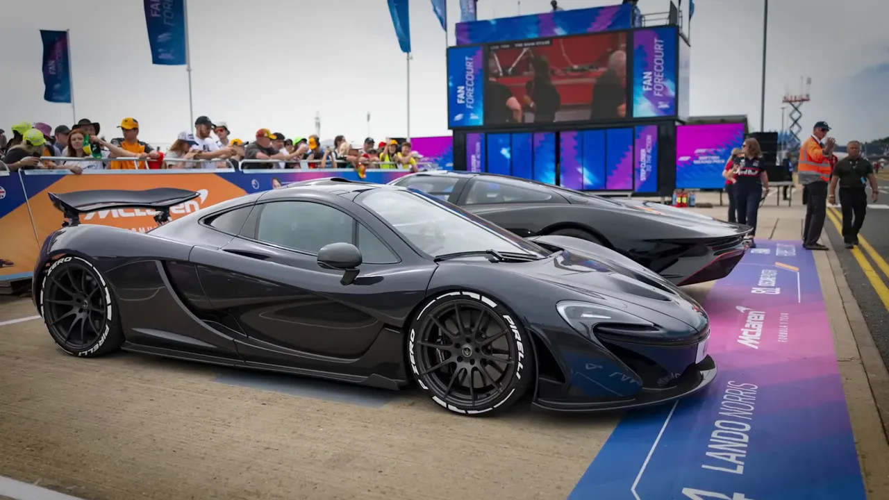 Side view of a gray McLaren supercar with track spectators and event signage in the background