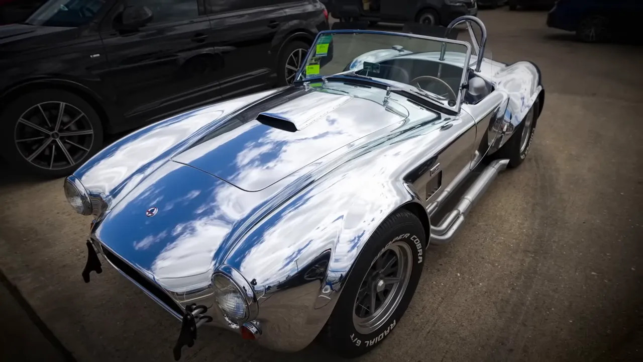 Silver Shelby Cobra 427 with roll bars parked indoors near other vehicles