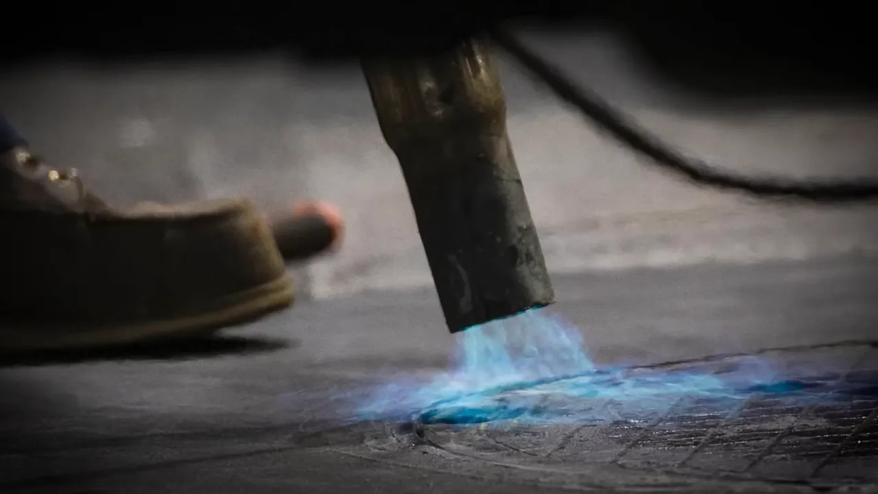 blue propane torch flame preheating a manhole cover on the track
