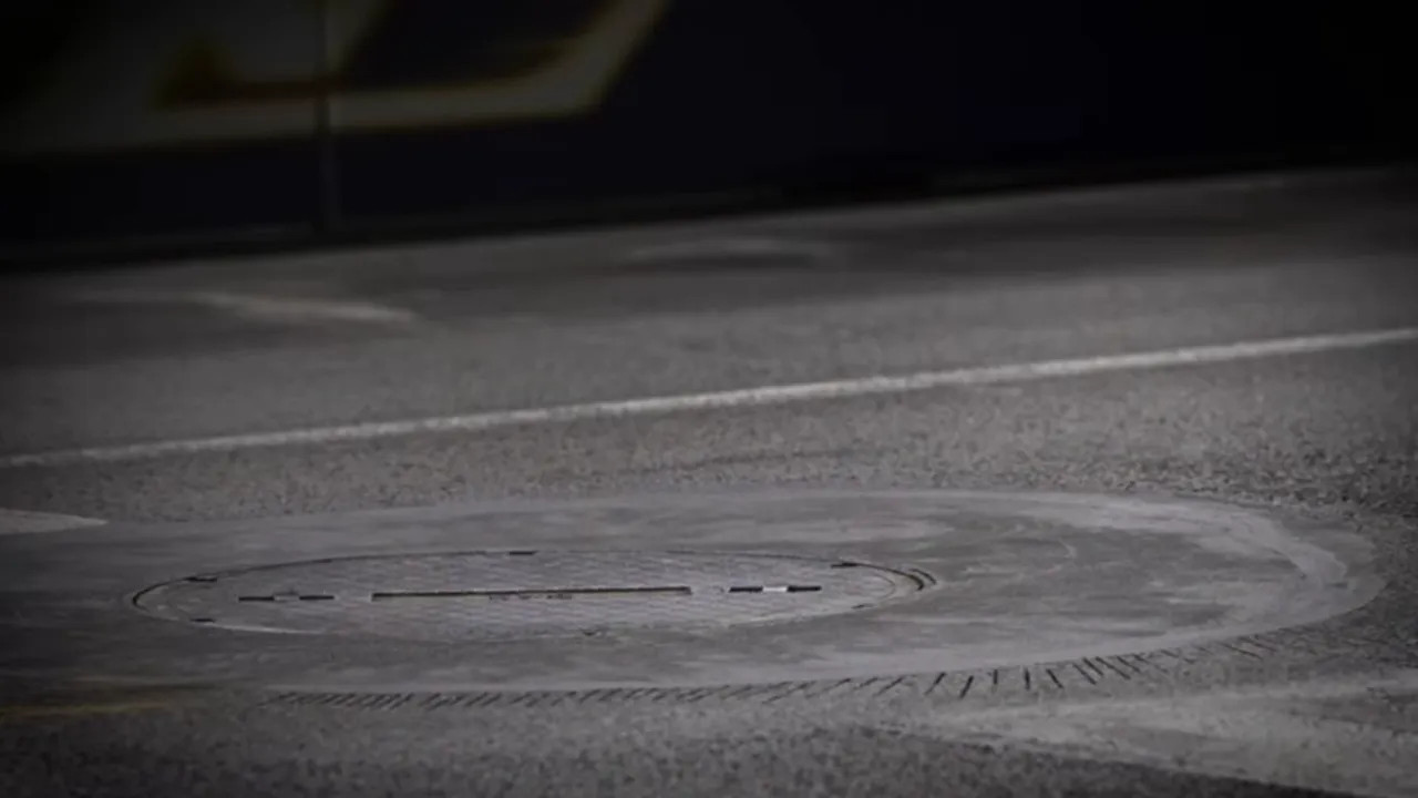 Close view of a circular manhole cover seated in the race surface with visible wear around the rim.