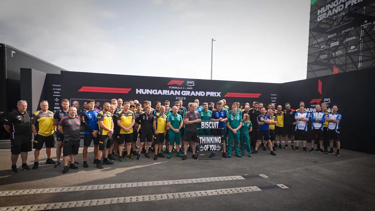 Formula 1 paddock staff gather for a group photo beneath a tribute sign