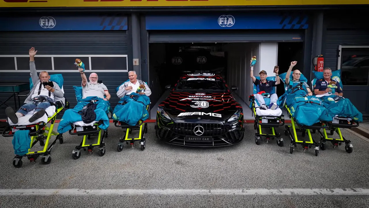 Patients in hospital stretchers pose with volunteers beside an FIA safety car garage