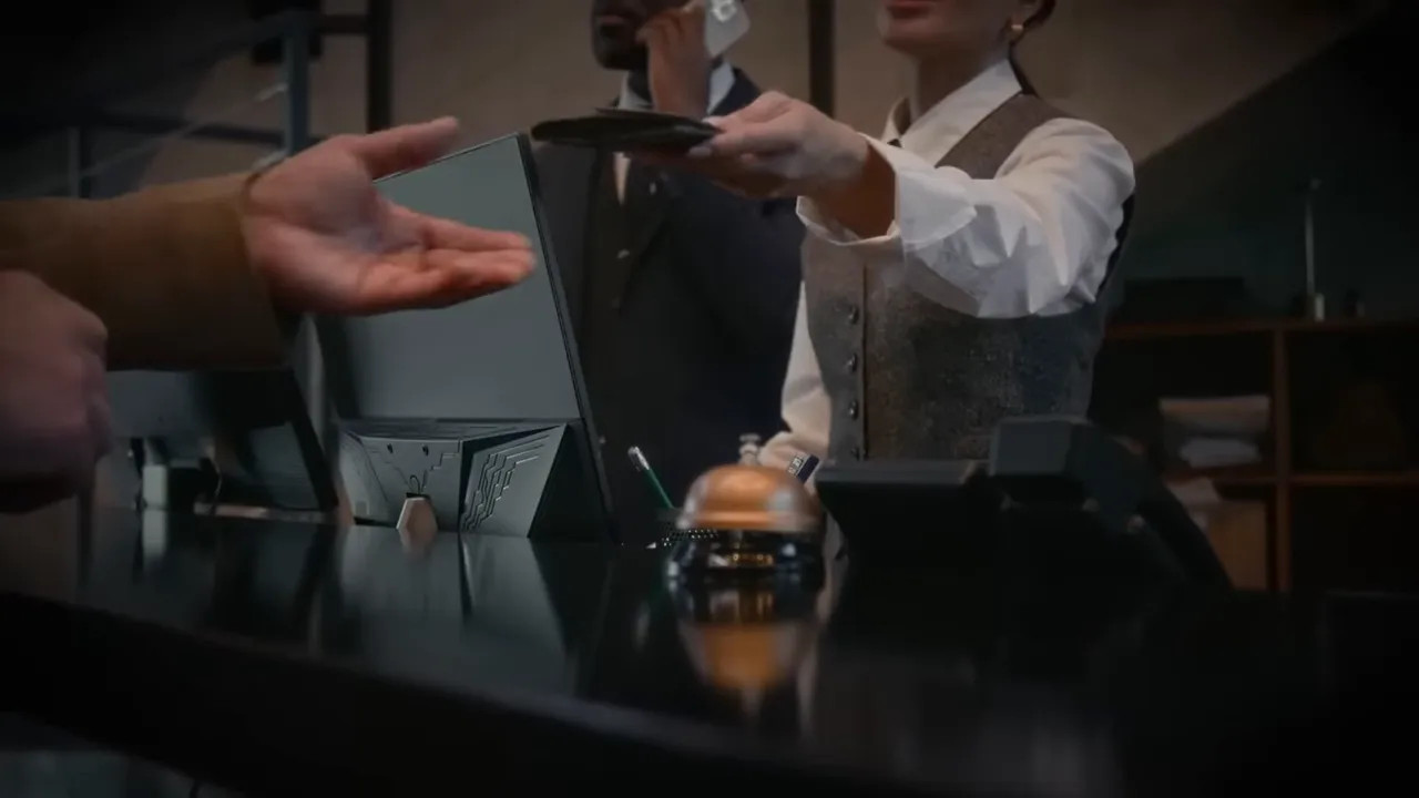 Hotel reception desk with staff handing a key card to a guest and a service bell visible