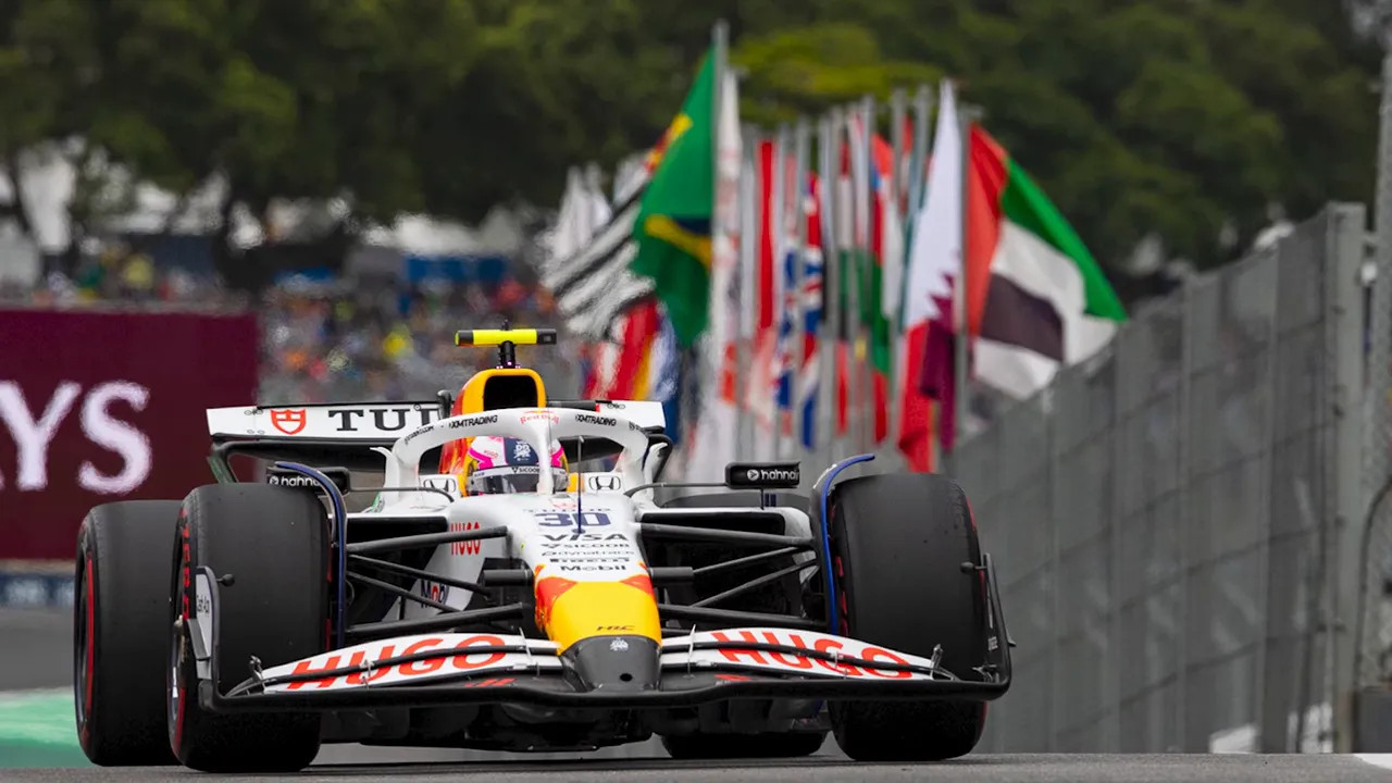 Open-wheel race car on track with rows of national flags in the background