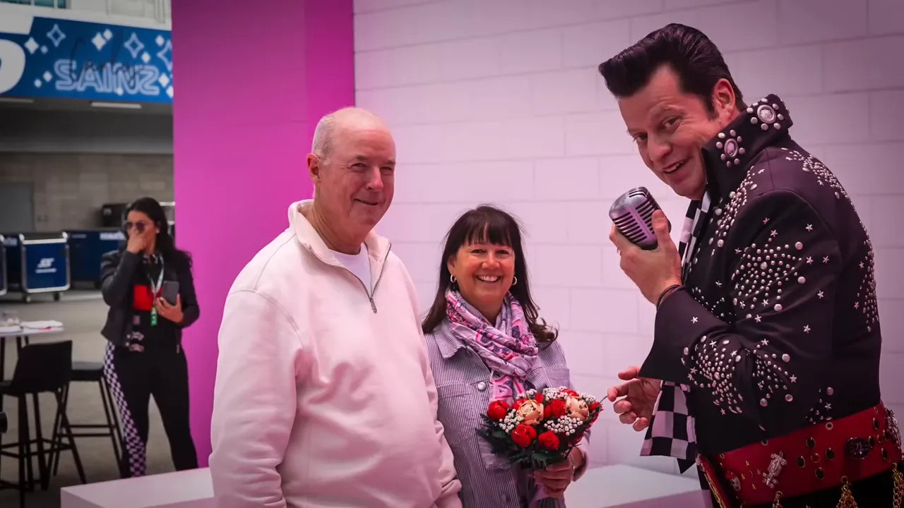 Entertainer posing with a smiling couple holding a bouquet inside an F1-themed neon chapel