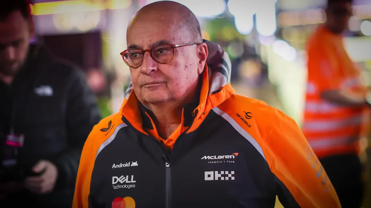 McLaren team member wearing orange jacket with visible sponsor logos in a busy paddock environment