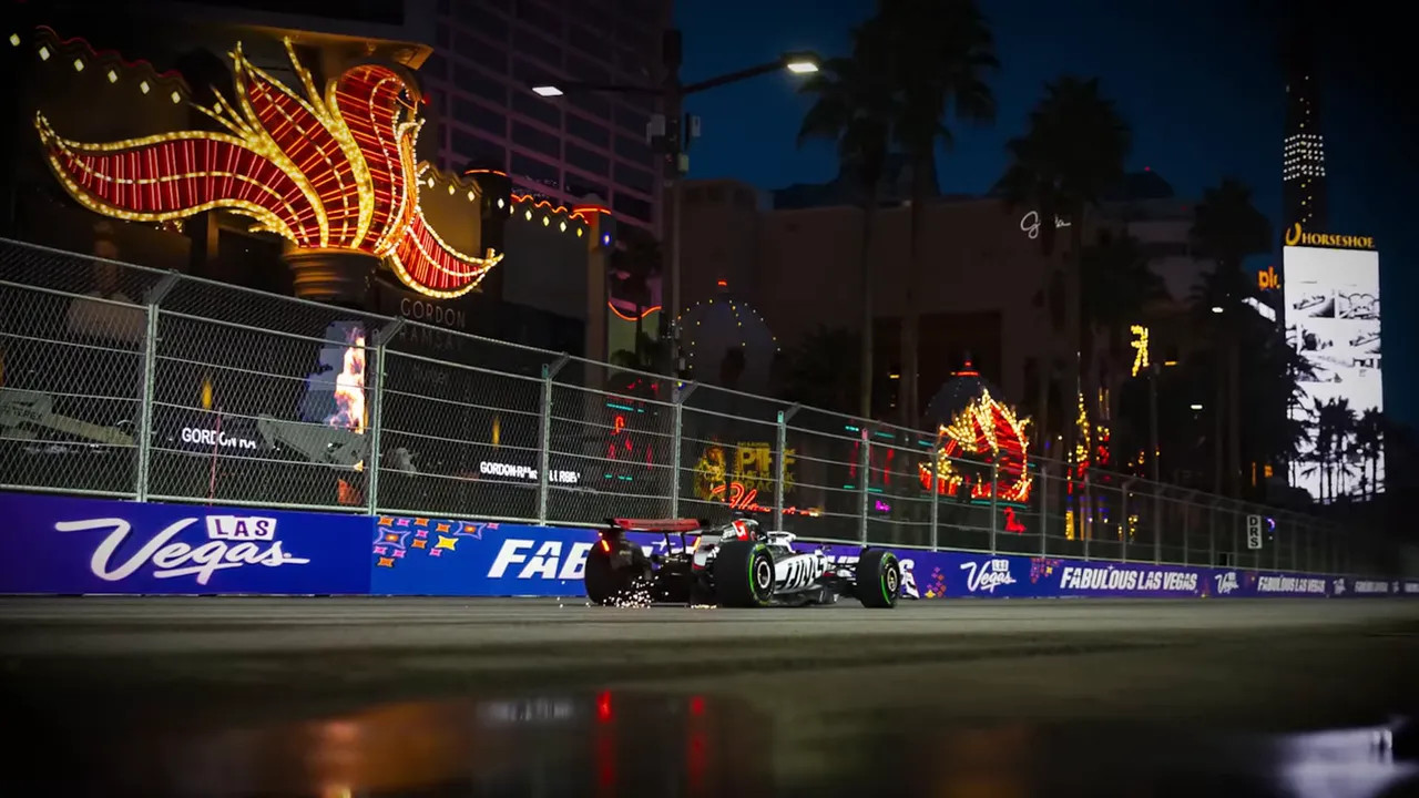 Wide shot of an F1 car on the Las Vegas street circuit at night with neon signage, reflections and sparks