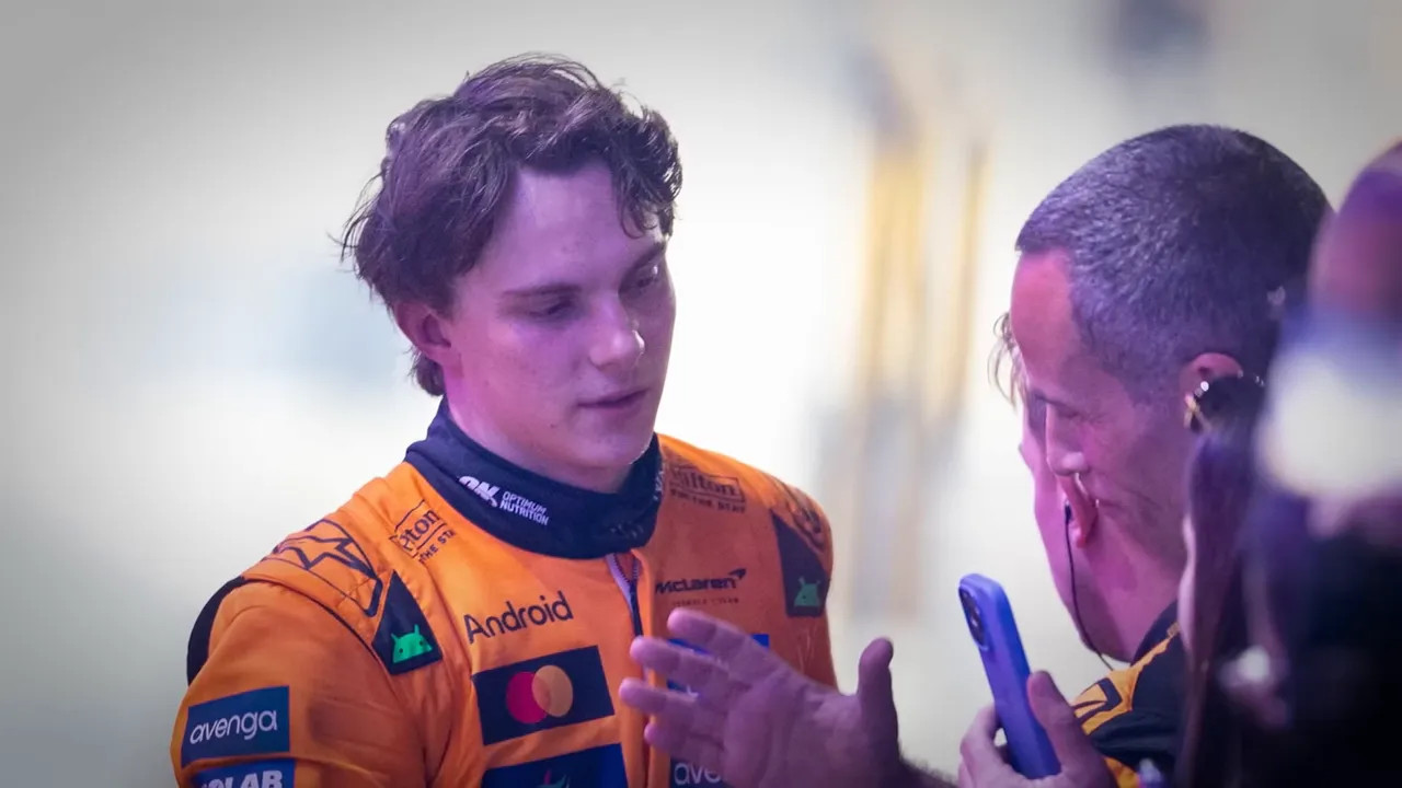 Subdued driver in orange McLaren race suit speaking with a team member in the paddock