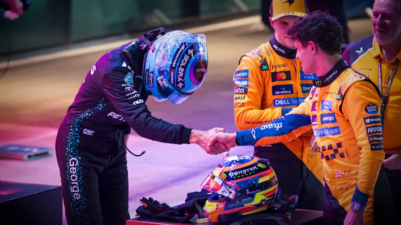 Two drivers exchanging a handshake in parc fermé while a team member and another driver look on