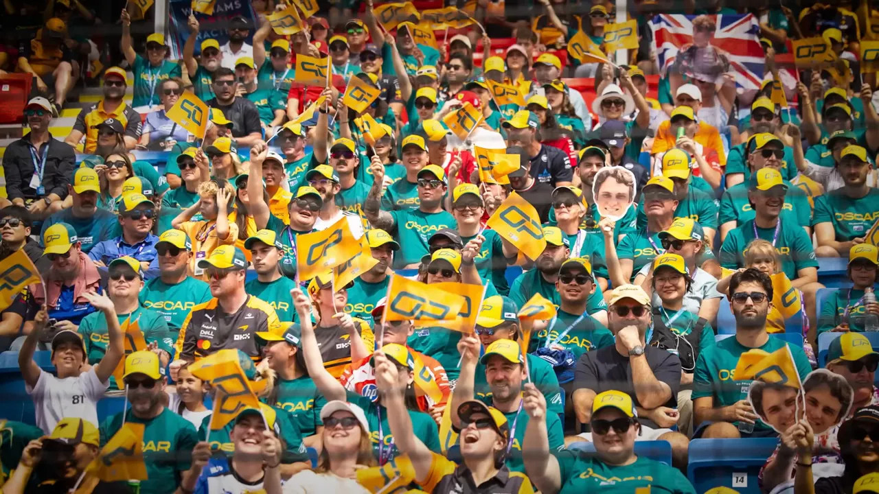 Crowd of Australian Grand Prix fans in green and gold shirts and caps waving yellow flags in the stands