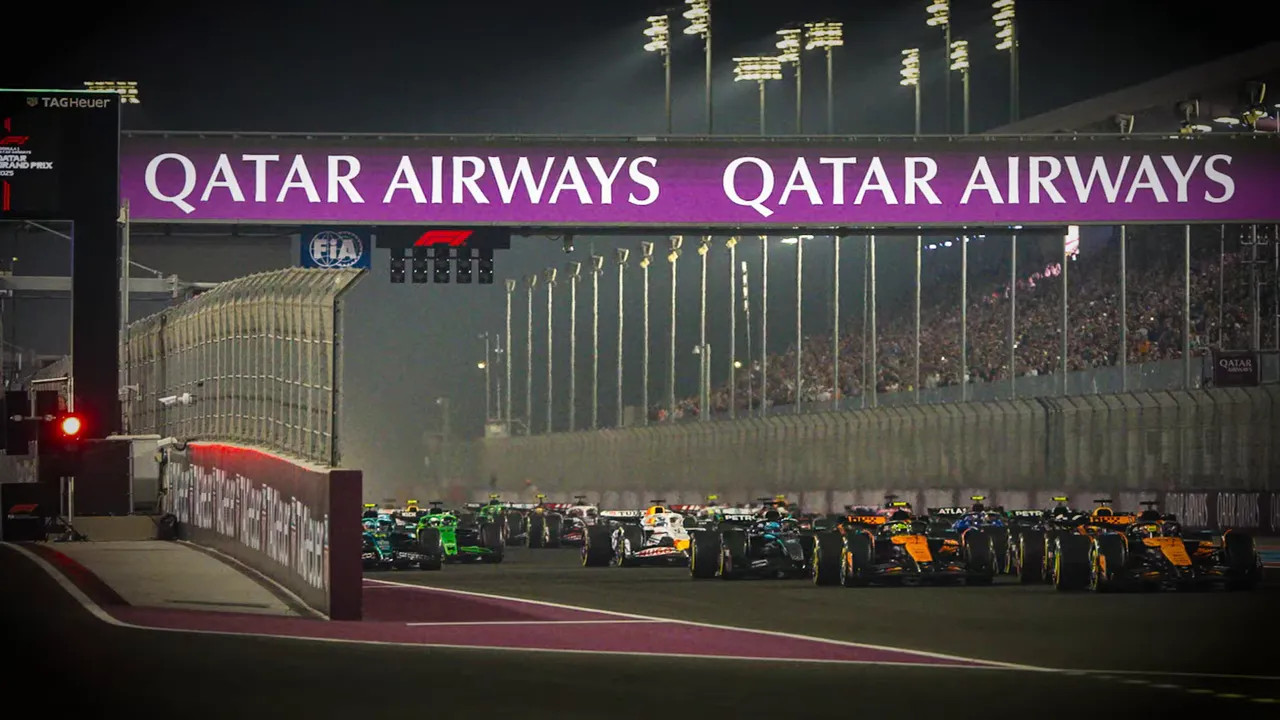Formula 1 cars lined up on a floodlit circuit beneath an Etihad bridge