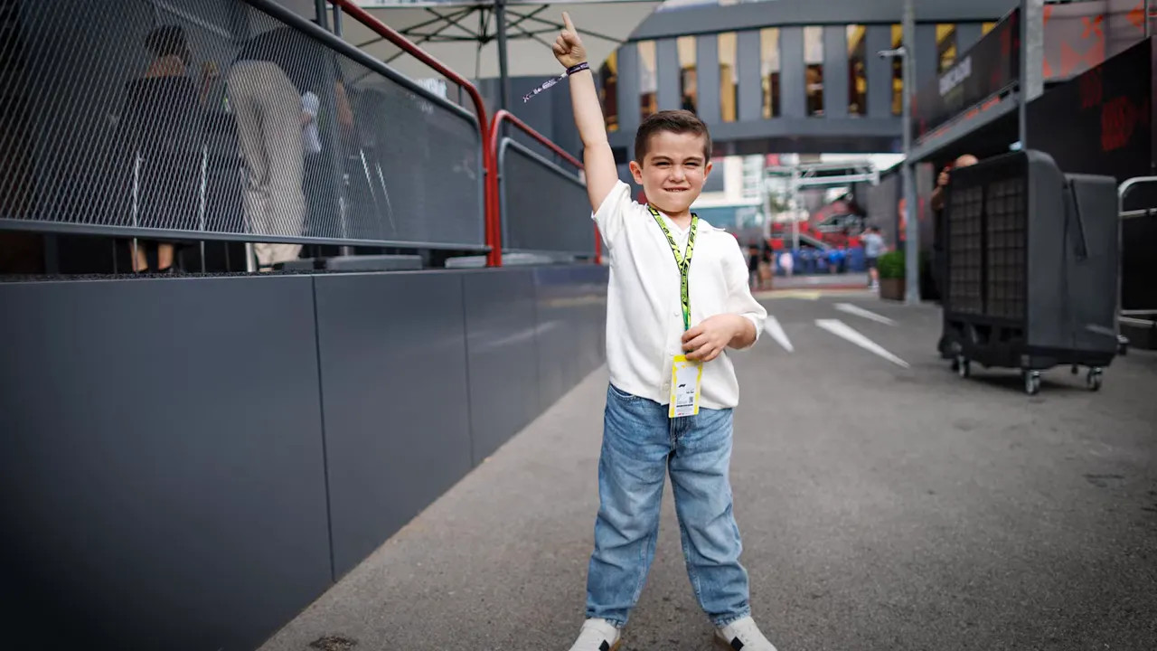 Young boy wearing a paddock pass and raising one arm in a circuit walkway