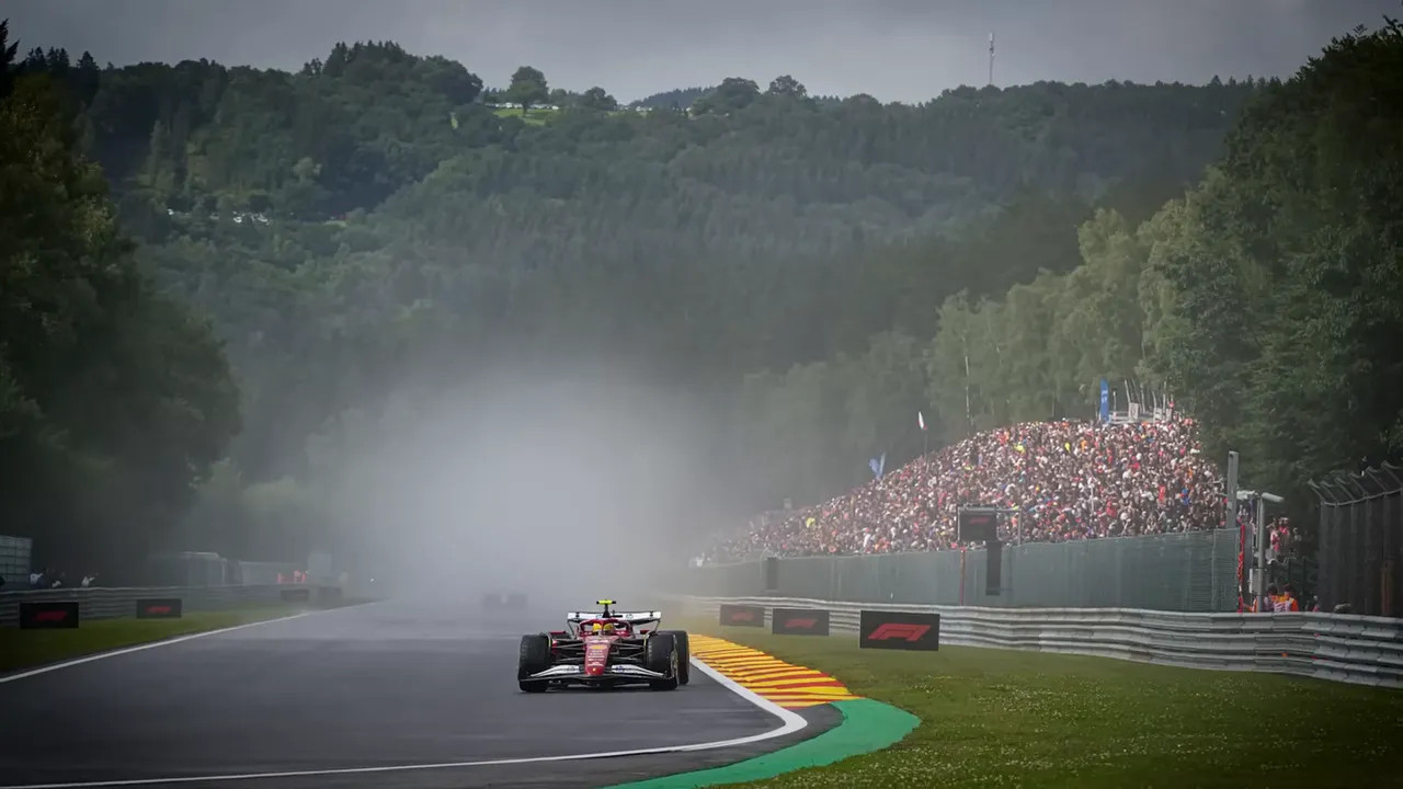 Formula 1 car driving through mist and spray with grandstand in the distance