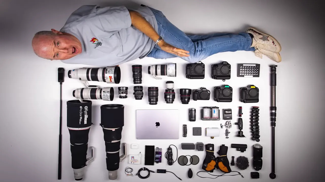 photographer lying beside a large layout of cameras lenses laptop and accessories