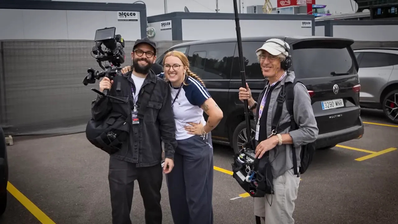 Three film crew members with a camera gimbal and boom microphone posing in a paddock car park