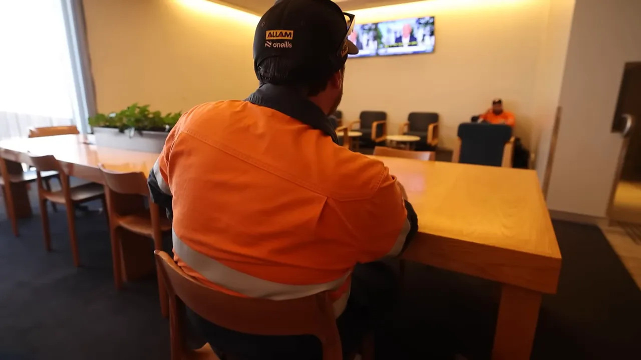 Passenger in high-visibility orange workwear seated in an airport lounge with seating in background (back view)