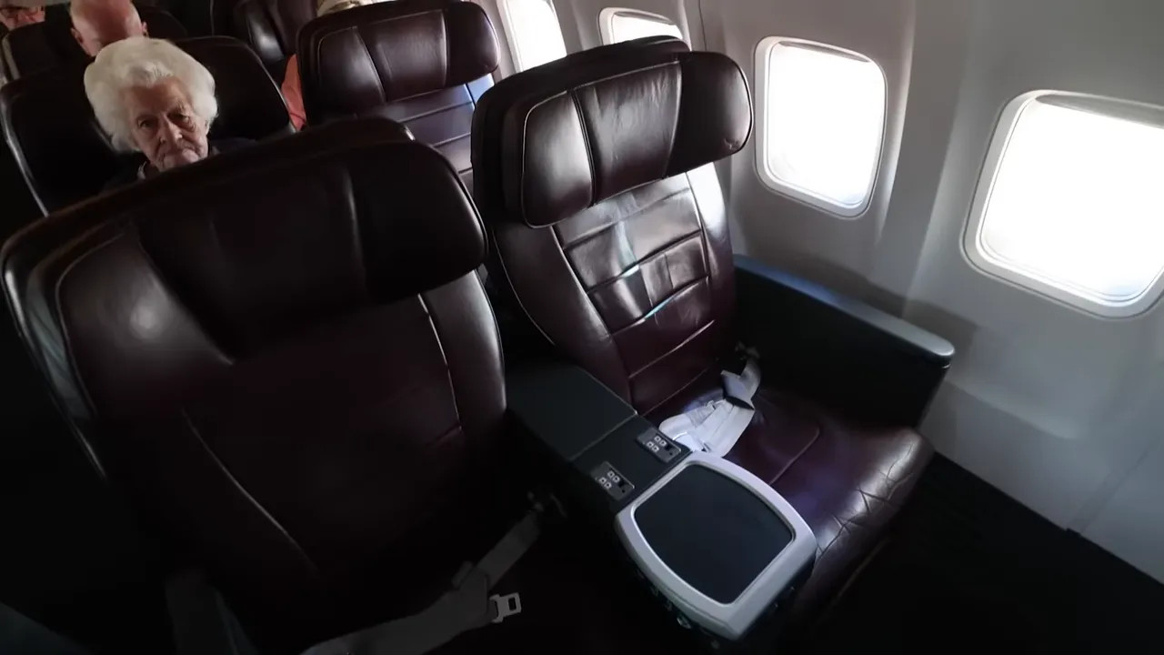 Two leather sit-up business class seats on a narrowbody aircraft showing the centre armrest, small tray area and in-seat power/USB ports