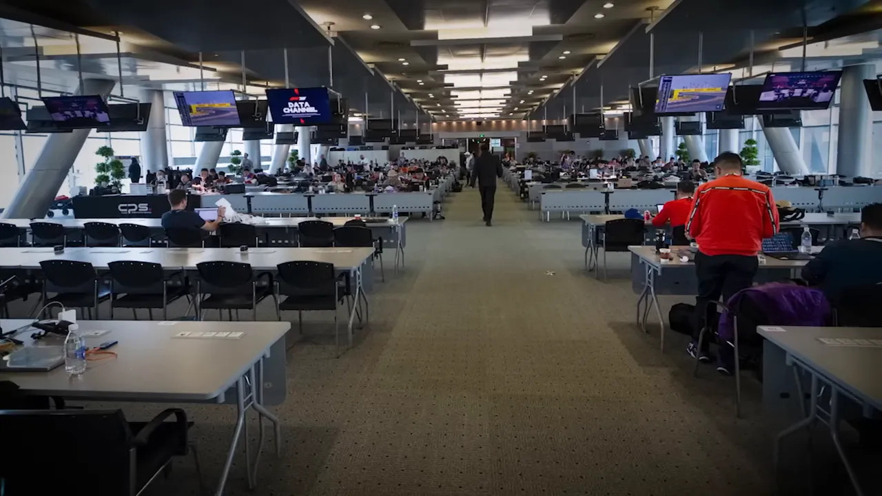 central aisle of a busy media centre showing desks, photographers and overhead monitors