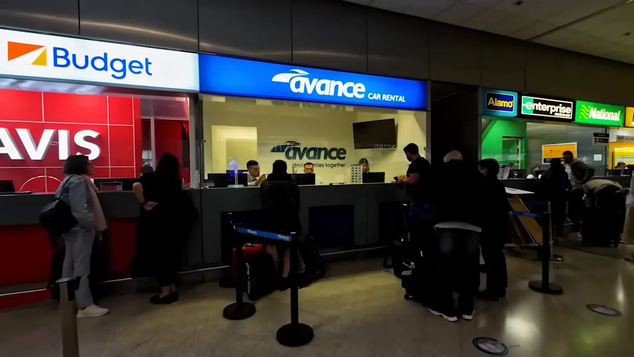 wide view of airport car rental counters with Budget, Avance, Alamo and Enterprise signage and customers