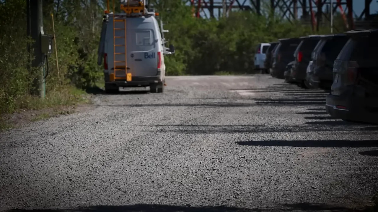 Road vehicles traveling along a gravel road lined with parked cars near the Canadian Grand Prix venue