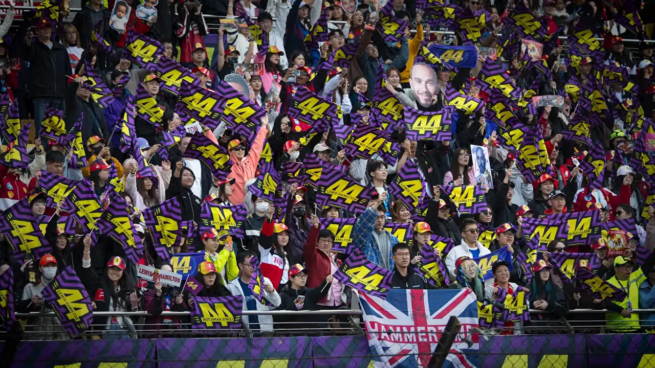 Large crowd of Formula 1 fans cheering with flags and signs in the stands