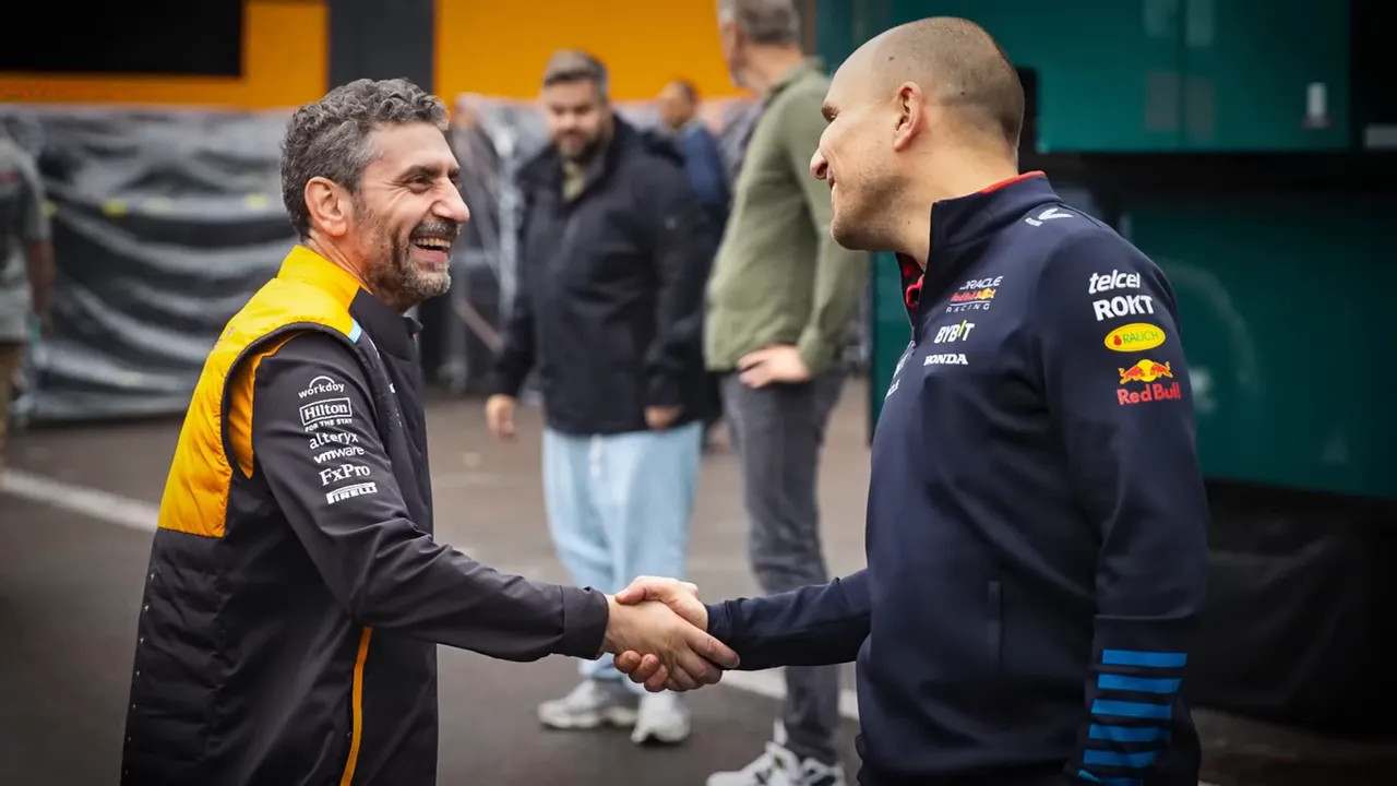 Two Formula 1 team members shaking hands outdoors on a race paddock walkway