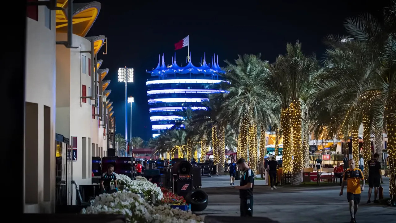 Nighttime paddock walkway with illuminated buildings and palm trees