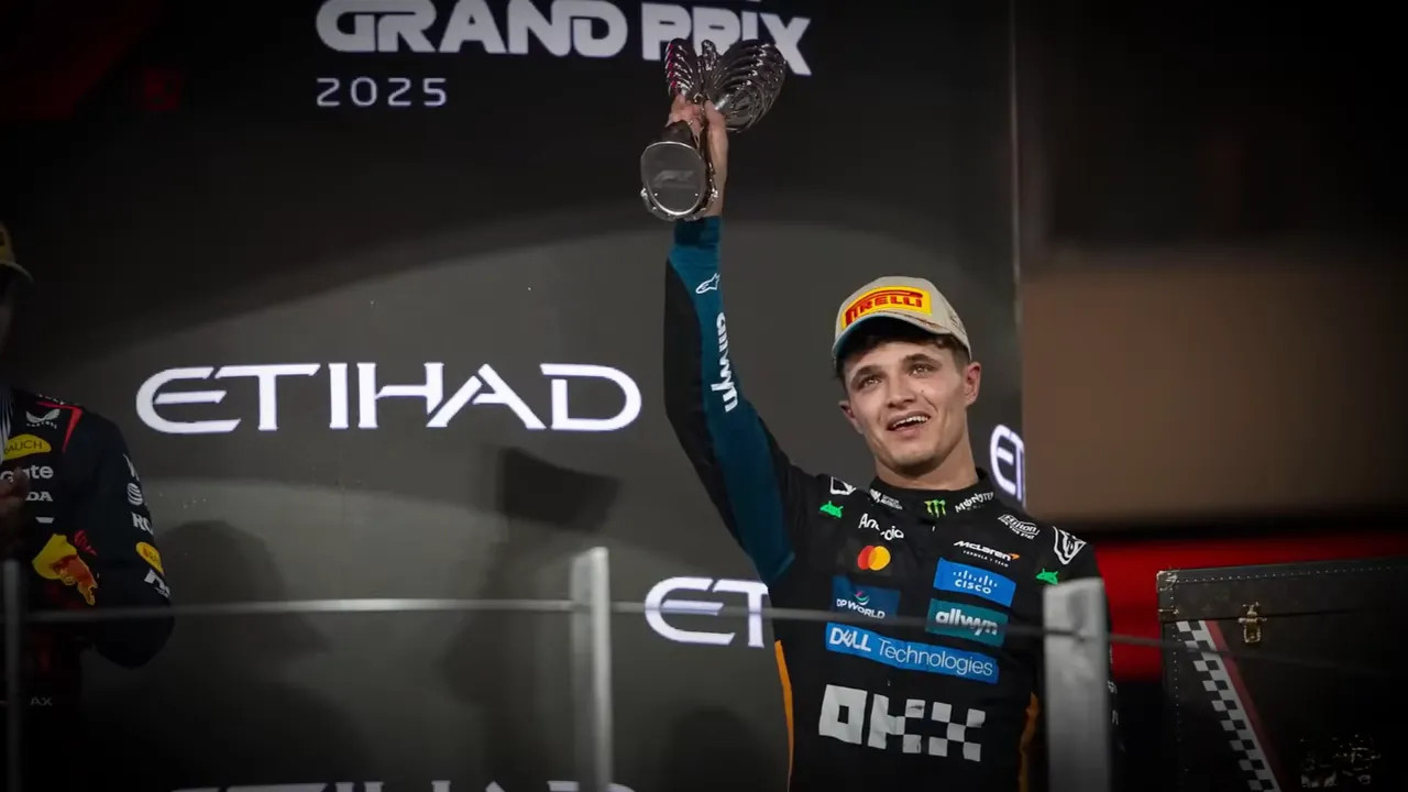 Driver raising a trophy on the Abu Dhabi Grand Prix podium at night with circuit branding behind.