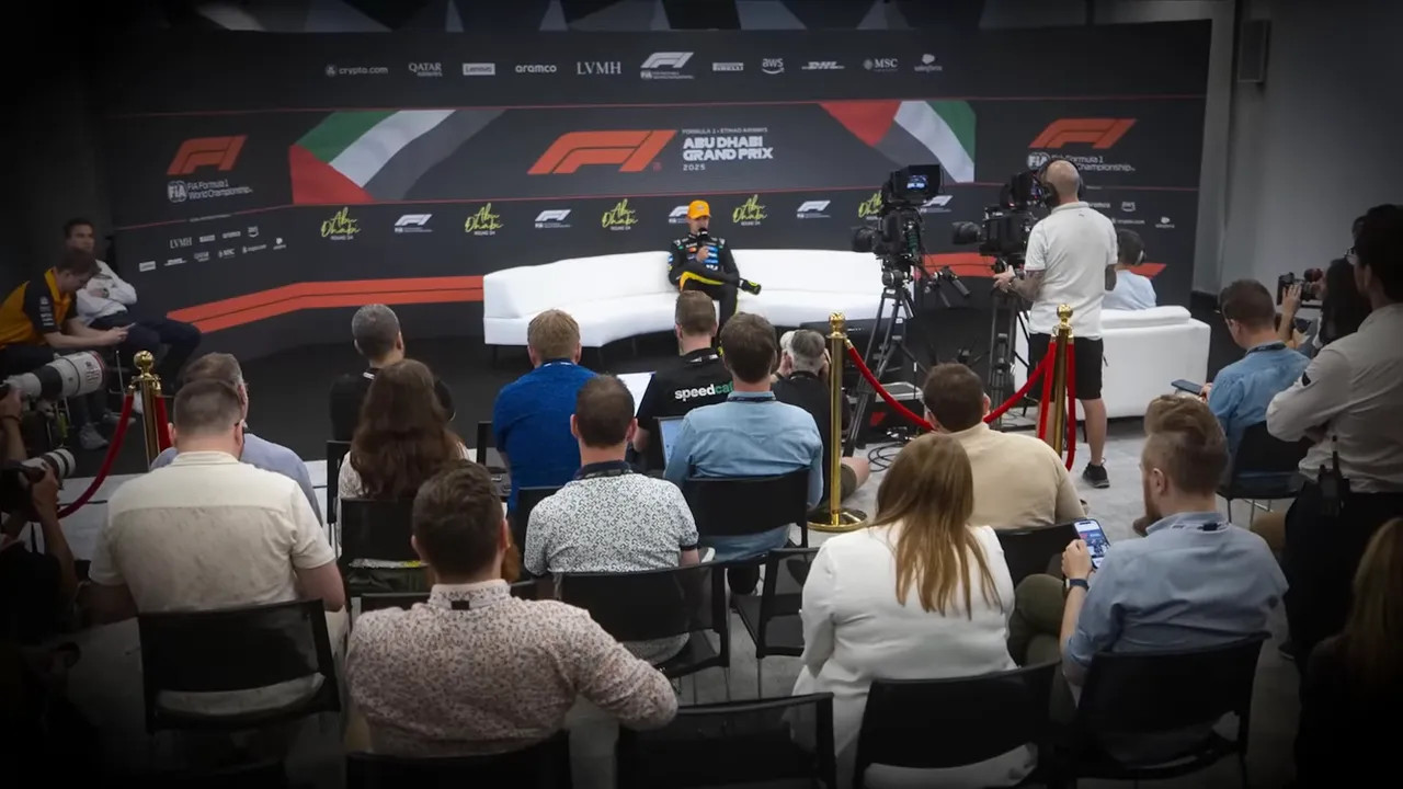 Press room with a driver seated on a white sofa facing rows of journalists, cameras and photographers.
