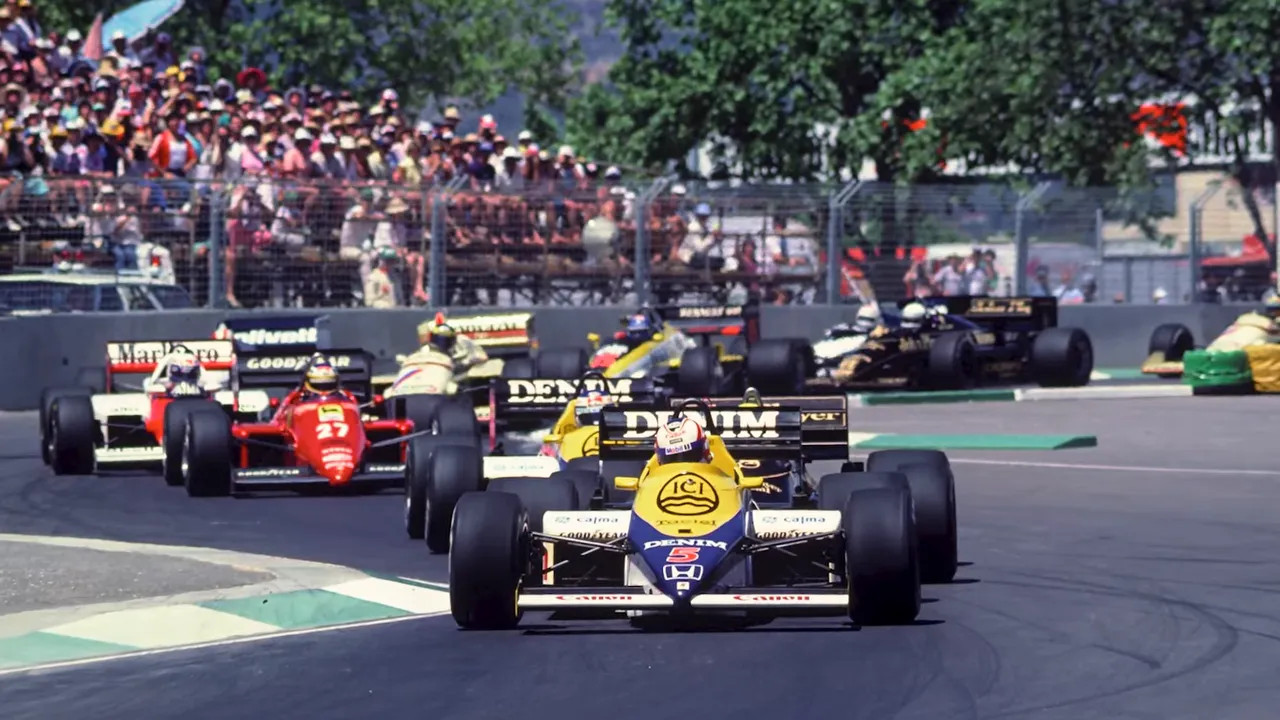 Pack of Formula 1 cars racing with large crowds along the circuit during the Adelaide Grand Prix era
