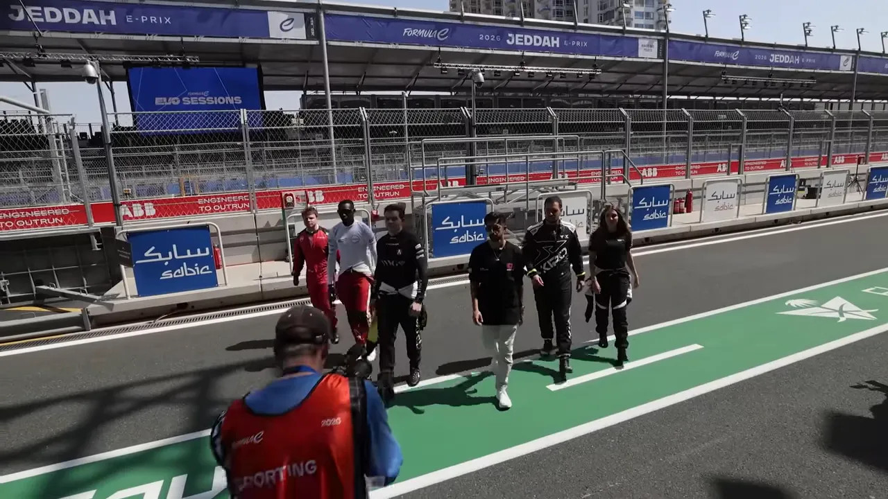 Group of creators and drivers walking down the Jeddah pit lane with grandstands and track fencing visible