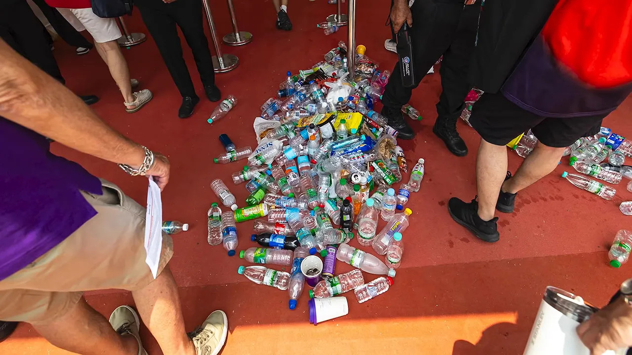 A large pile of plastic bottles on a red floor surrounded by people at an entrance