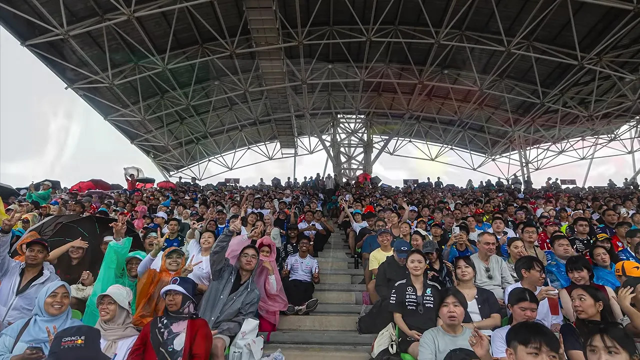 Fans in the grandstand holding Italian and Malaysian flags with their arms raised