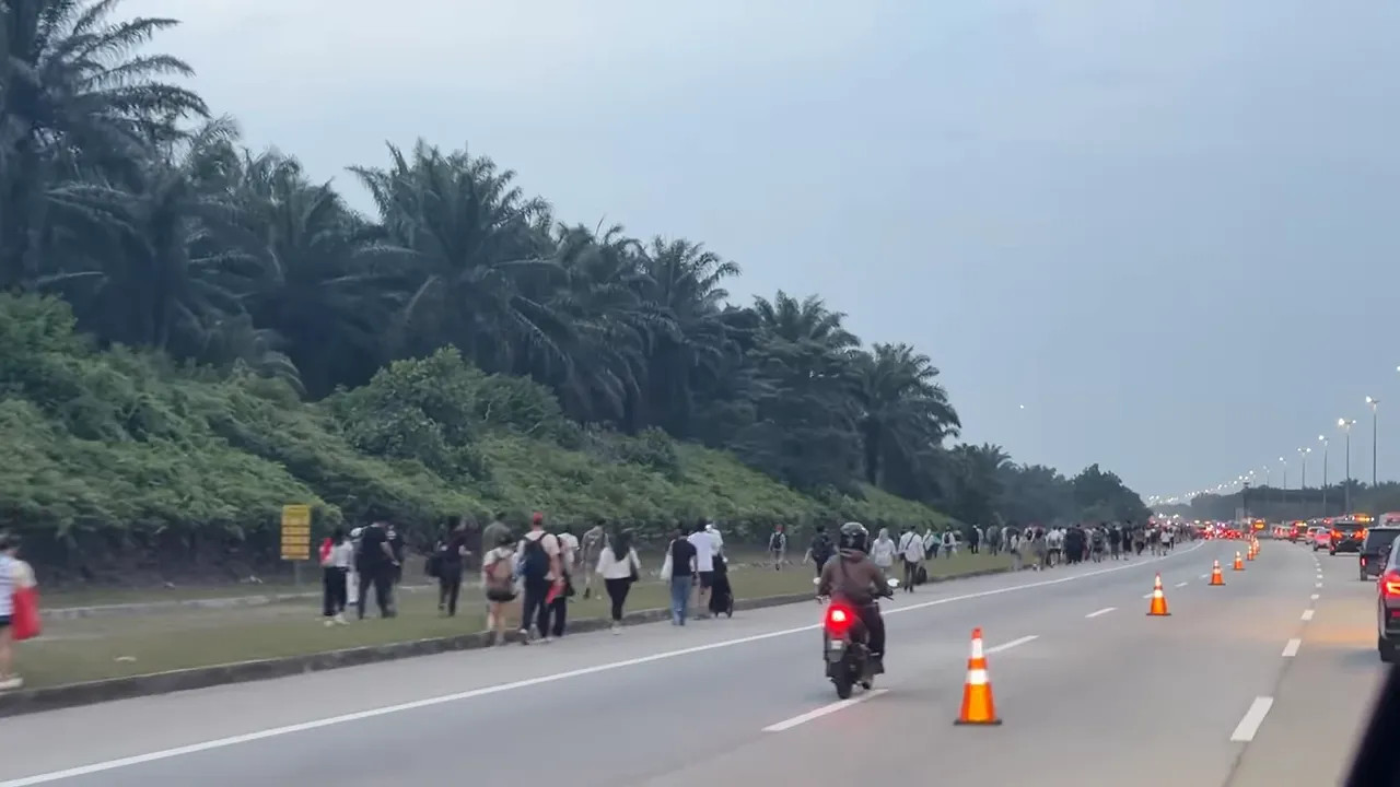 People walking beside a multilane road with cars, a motorcycle and traffic cones