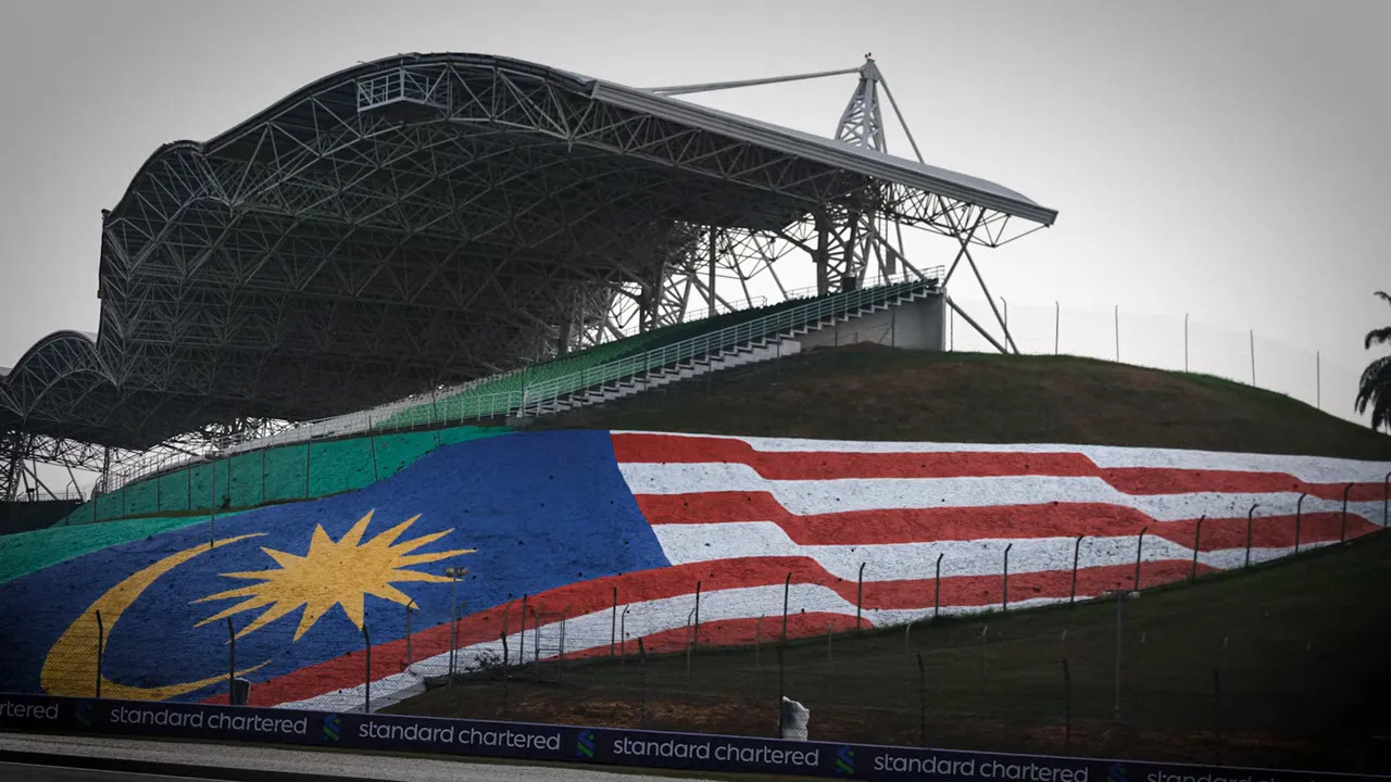 Large Malaysian flag painted on a grassy bank beneath a Sepang grandstand