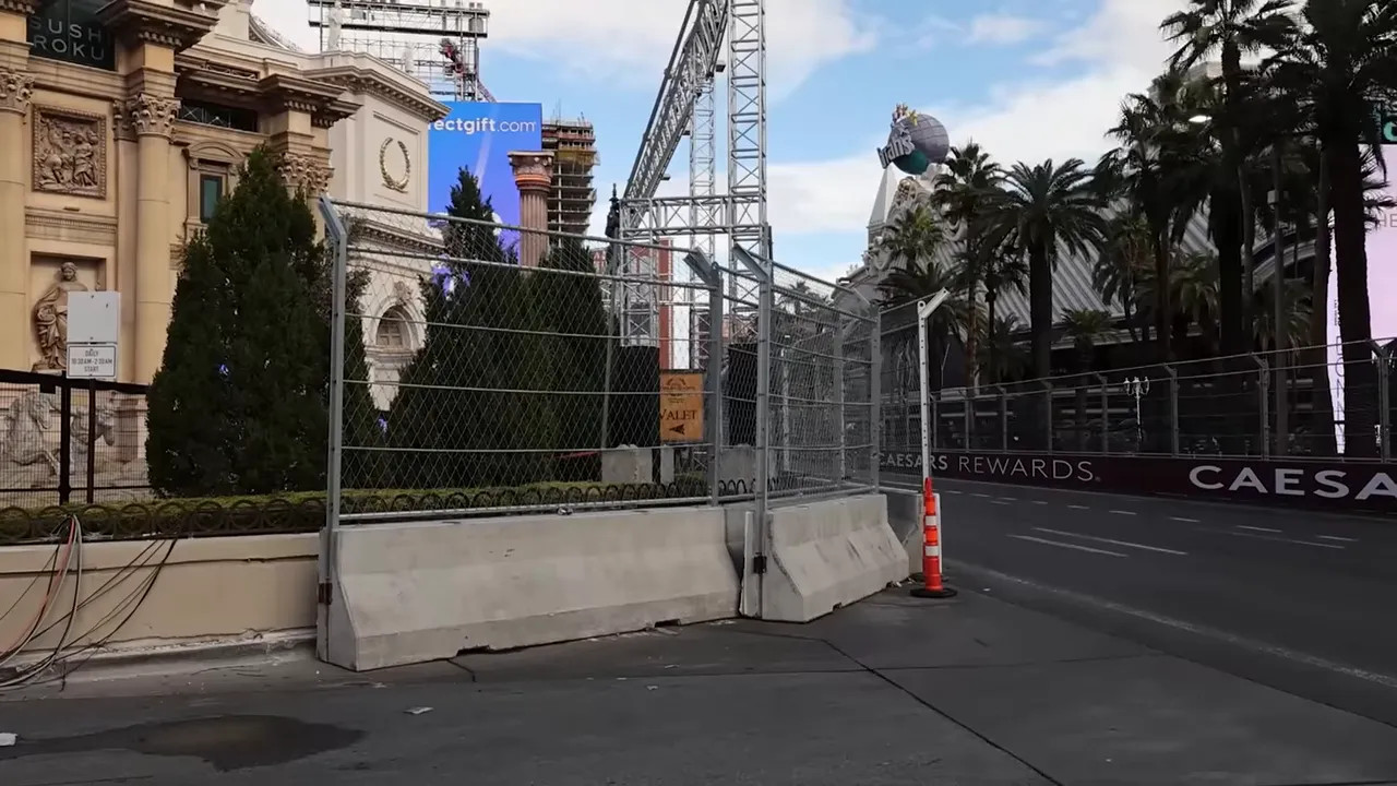 Temporary spectator fencing and concrete barriers on the Las Vegas Strip forming the race perimeter, with a traffic cone at the corner.