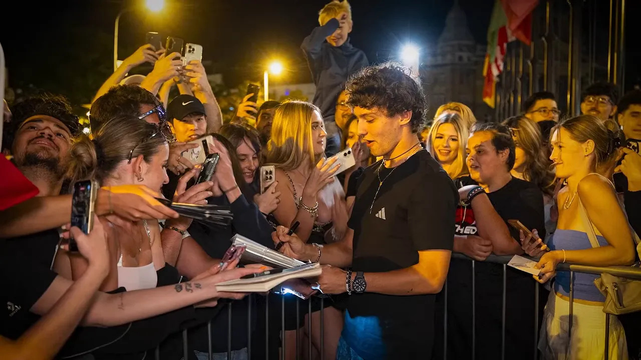 Antonelli signing items for a crowd of fans behind barriers at night