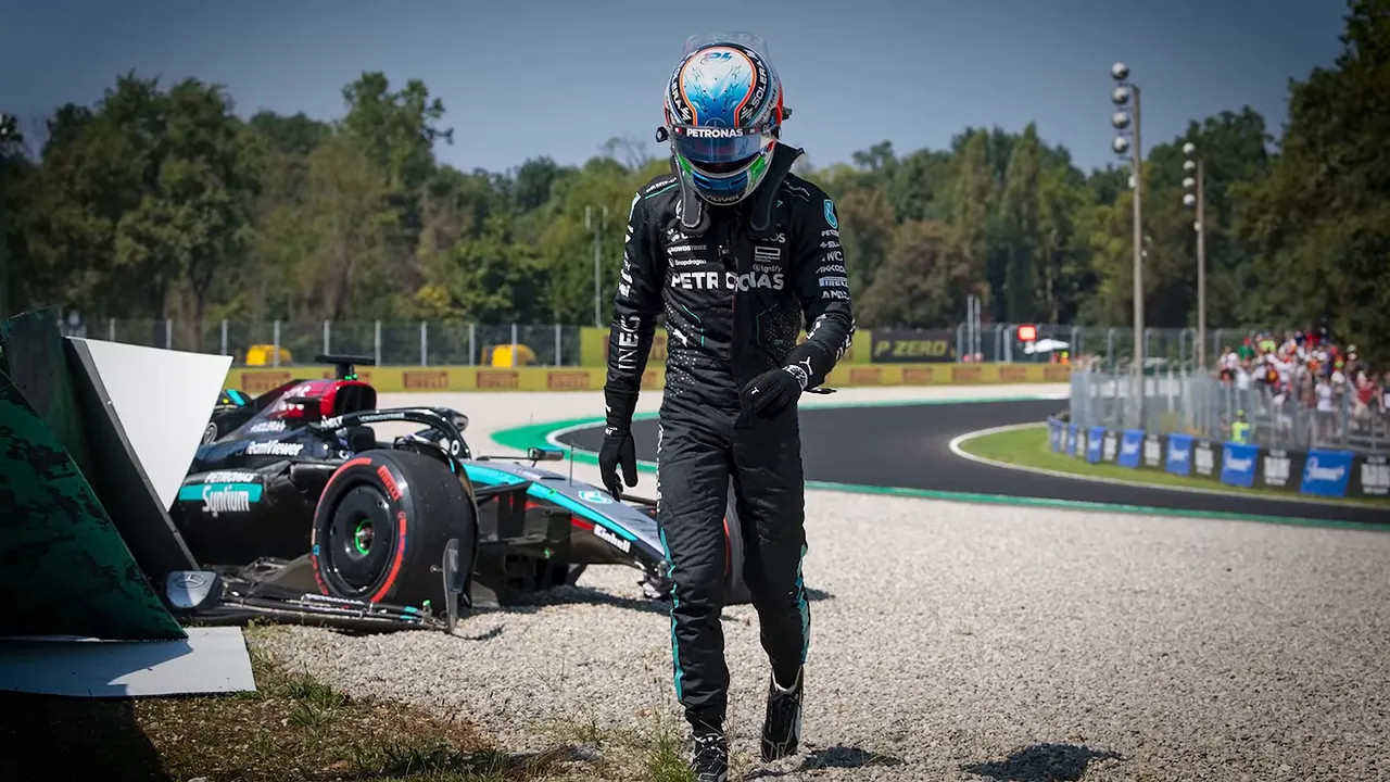 Antonelli walking through gravel with a damaged Mercedes beside the barriers behind him