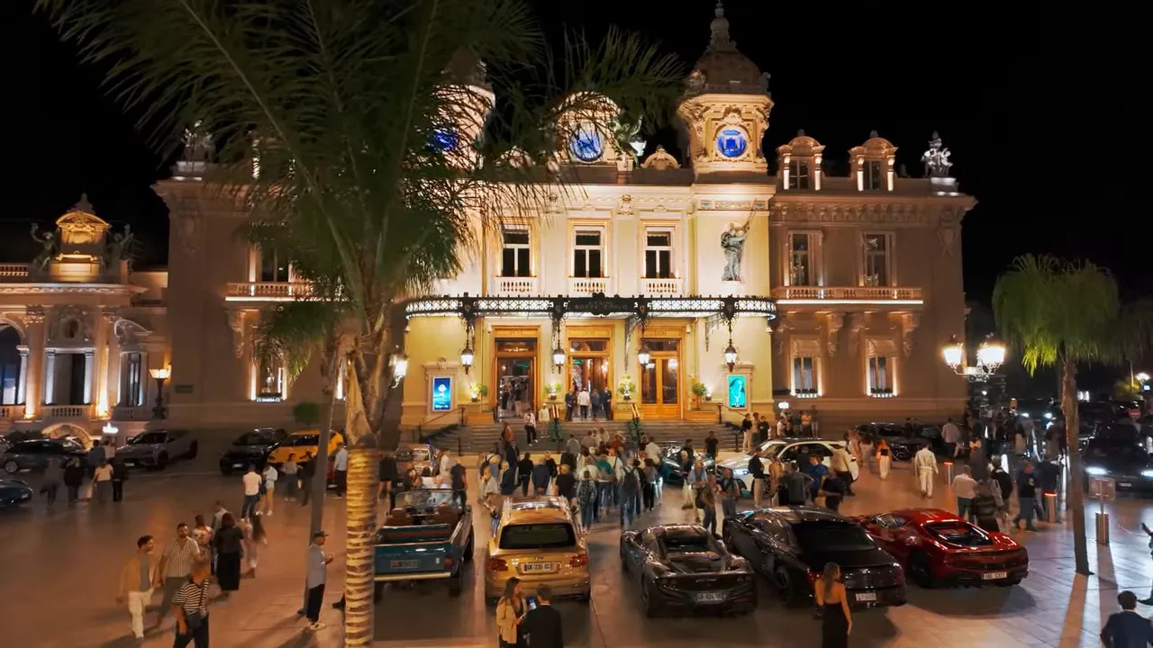 Monte Carlo casino illuminated at night with crowds and parked cars outside