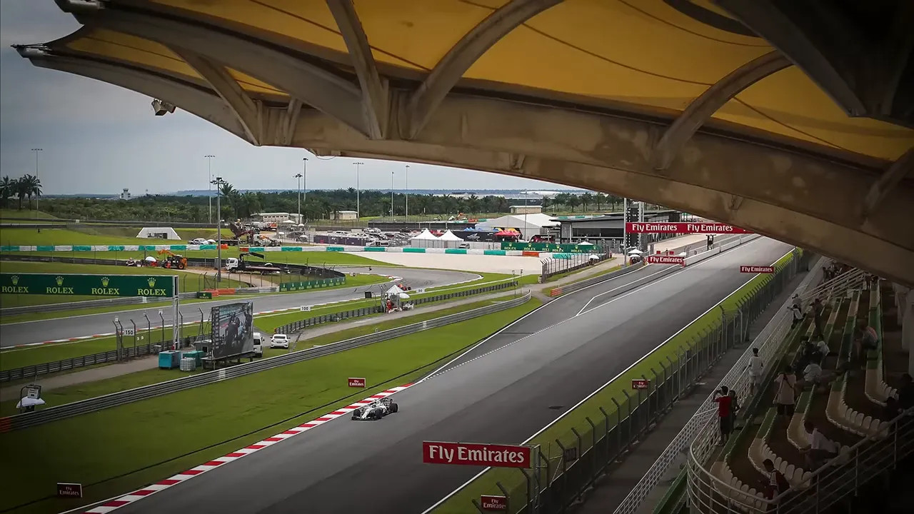 Formula 1 car driving at Sepang International Circuit beneath grandstand roof