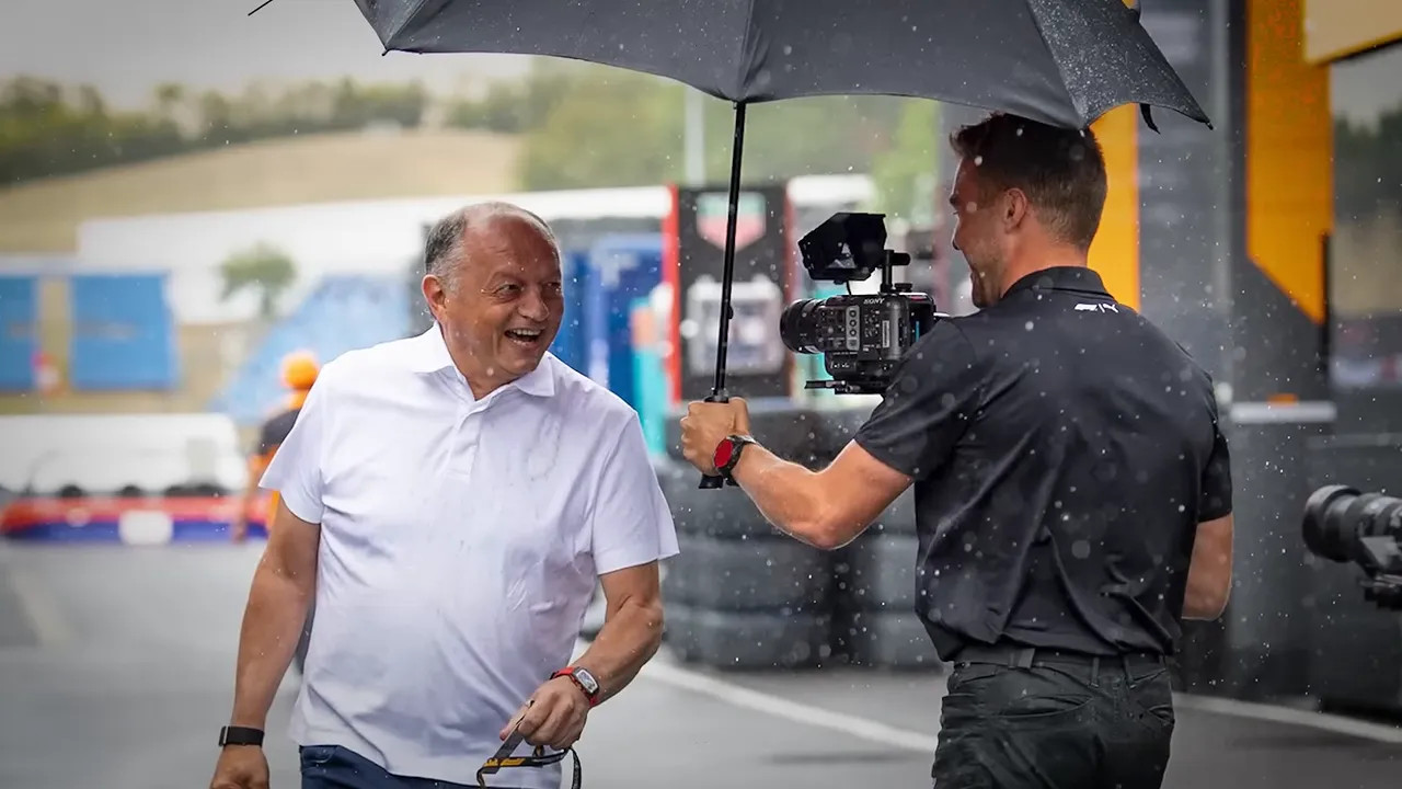 Fred Vasseur standing under an umbrella in heavy rain in the paddock
