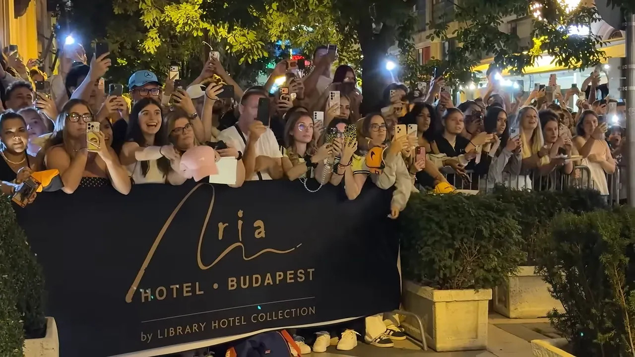 Large crowd gathered outside Aria Hotel Budapest holding phones and merchandise